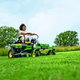 Kobieta na zielonej, zero-skrętnym traktorku koszącym, który jest rodzajem kosiarki bębnowej, z łatwością pielęgnuje trawnik.