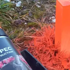Pomarańczowe paliki geodezyjne, jeden z nich otoczony farbą, obok puszki z napisem SOPPEC CONSTRUCTION.