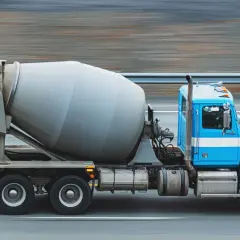 Niebieska ciężarówka z obracającym się bębnem, przewożąca beton z gruszki, pędzi po drodze.