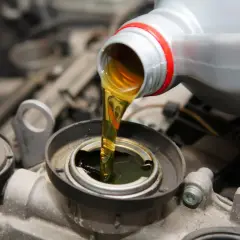 Wlewanie oleju do silnika Hatz Diesel. Płynny złoty olej spływa z szarej butelki do otworu silnika.