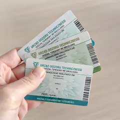 Ręka trzyma kilka zaświadczeń kwalifikacyjnych Urzędu Dozoru Technicznego, potwierdzających uprawnienia na zwyżki.