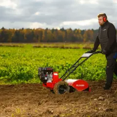 Mężczyzna w słuchawkach ochronnych prowadzi glebogryzarkę, która spulchnia ziemię, napotykając na swojej drodze kamienie.