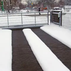 Śnieg na kostce brukowej przy bramie. Widać, że ogrzewanie kostki brukowej działa, bo śnieg stopił się na środku, tworząc wolne od lodu ścieżki.