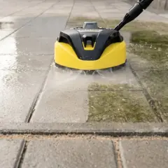 Czyszczenie kostki brukowej myjką ciśnieniową. Widać wyraźną różnicę między umytą a brudną powierzchnią.