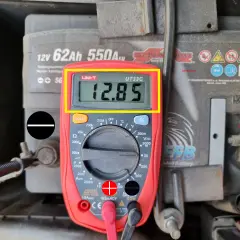 Multimetr pokazuje 12.85V, co jest wynikiem pomiaru napięcia elektrycznego akumulatora samochodowego.