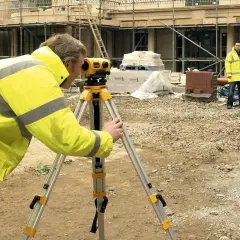 Geodeta używa niwelatora do precyzyjnych pomiarów na budowie. Praca wre, a budowa niwelatora jest kluczowa dla dokładności.