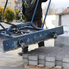 Ręczna zagęszczarka podnosi kostkę brukową. Pracownik w kombinezonie przygotowuje teren do układania nawierzchni.
