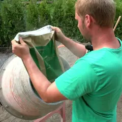 Mężczyzna w zielonej koszulce wsypuje zawartość worka do betoniarki, przygotowując masę.