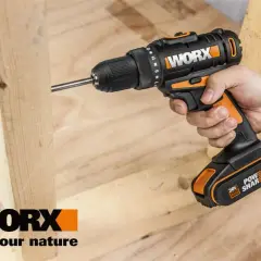 Dłoń trzyma wkrętarkę Worx, która wkręca śrubę w drewno. Worx to marka narzędzi dla majsterkowiczów.