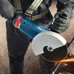 Pracownik w rękawicach zakłada tarczę na szlifierkę kątową Bosch, przygotowując się do cięcia metalu. Iskry sypią się podczas pracy.