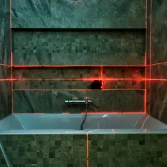 Laser krzyżowy wyznacza linie, pomagając jak wyznaczyć kąt prosty na podłodze. W łazience z wanną i nowoczesnymi płytkami.
