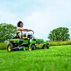 Kobieta na zielonej, zero-skrętnym traktorku koszącym, który jest rodzajem kosiarki bębnowej, z łatwością pielęgnuje trawnik.