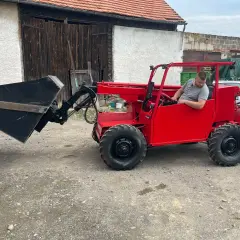 Czerwona ladowarka teleskopowa z operatorem gotowa do pracy na podwórzu.