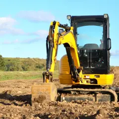 Żółta minikoparka na placu budowy. Operator przygotowuje teren do prac ziemnych, wykorzystując sprzęt do kopania i przemieszczania ziemi.
