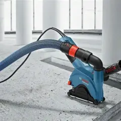 Narzędzie Bosch wykonuje bruzdowanie pod kable w betonie. Wąż odkurzacza odprowadza pył.