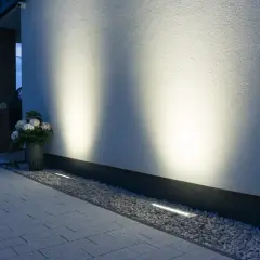 Nowoczesne oświetlenie placu budowy podkreśla architekturę domu. Dyskretne lampy wbudowane w żwir i podjazd tworzą nastrojową atmosferę.