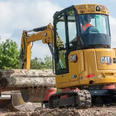 Minikoparka CAT 302.7 pracuje przy kopaniu fundamentów, podnosząc drewniane belki.
