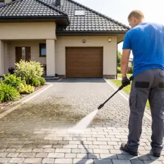 Mężczyzna z myjką ciśnieniową wykonuje czyszczenie kostki brukowej przed domem.