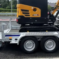 Żółta minikoparka na przyczepie, gotowa do transportu. Jej waga jest znacząca, ale przyczepa jest solidna.