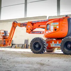 Pomarańczowy wysięgnik budowlany z podestem roboczym czeka na placu budowy, gotowy do pracy na wysokości.