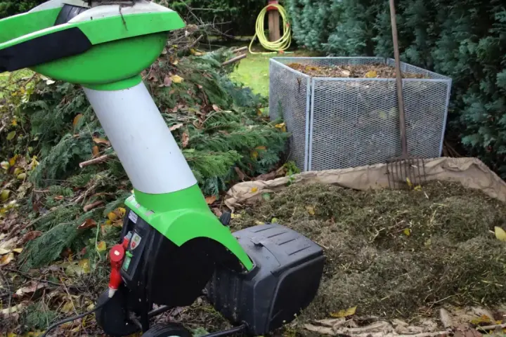 Zielona maszyna do rozdrabniania drewna pracuje w ogrodzie, przetwarzając gałęzie na kompost.