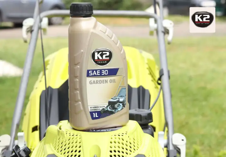 Butelka oleju K2 SAE 30 Garden Oil do kosiarki spalinowej, stojąca na żółtej obudowie maszyny.