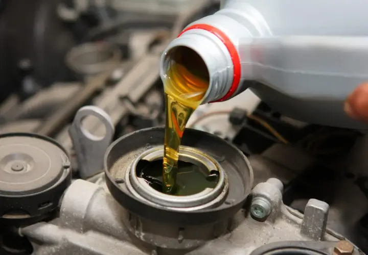 Wlewanie oleju do silnika Hatz Diesel. Płynny złoty olej spływa z szarej butelki do otworu silnika.