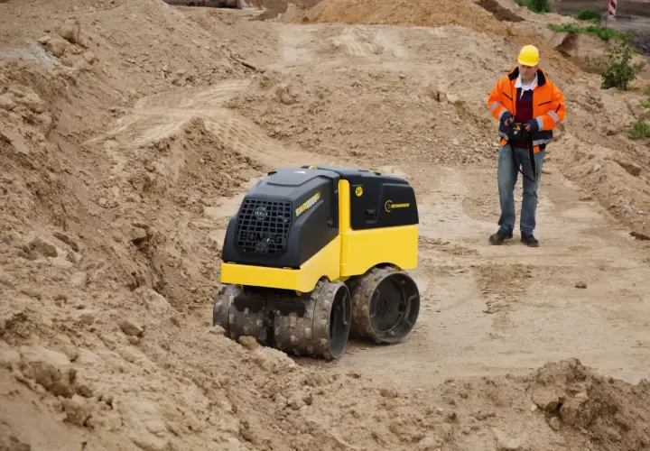 Na budowie pracuje operator z pilotem, sterując maszyną Bomag BMP 8500.