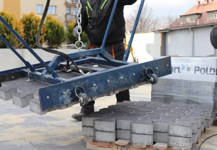 Ręczna zagęszczarka podnosi kostkę brukową. Pracownik w kombinezonie przygotowuje teren do układania nawierzchni.