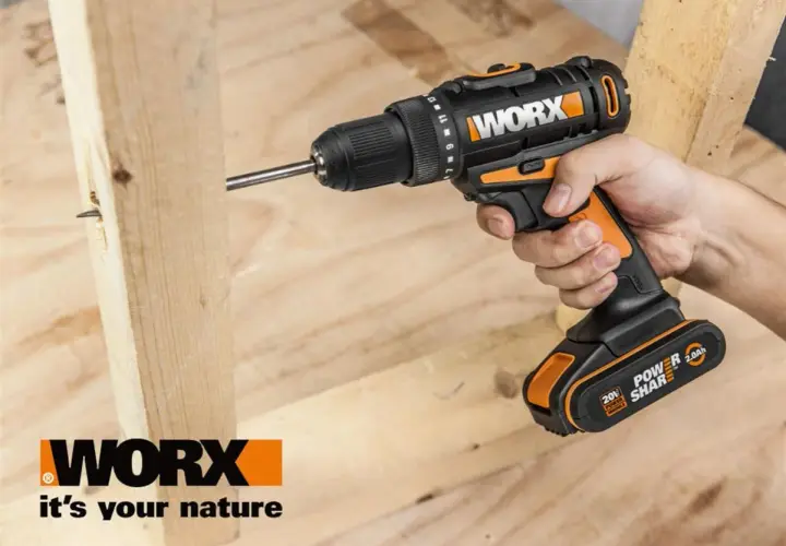 Dłoń trzyma wkrętarkę Worx, która wkręca śrubę w drewno. Worx to marka narzędzi dla majsterkowiczów.