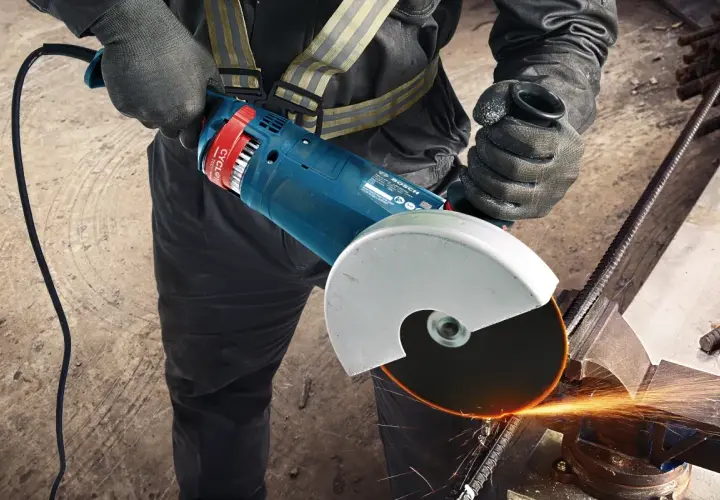 Pracownik w rękawicach zakłada tarczę na szlifierkę kątową Bosch, przygotowując się do cięcia metalu. Iskry sypią się podczas pracy.