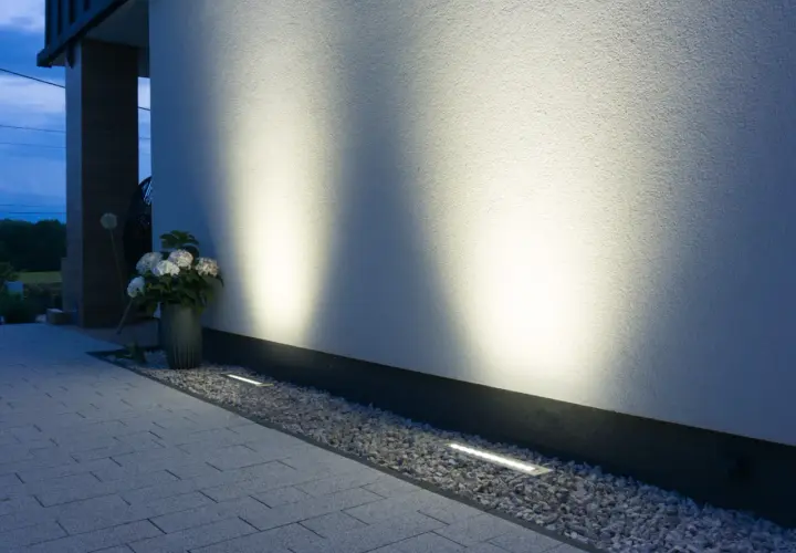Nowoczesne oświetlenie placu budowy podkreśla architekturę domu. Dyskretne lampy wbudowane w żwir i podjazd tworzą nastrojową atmosferę.