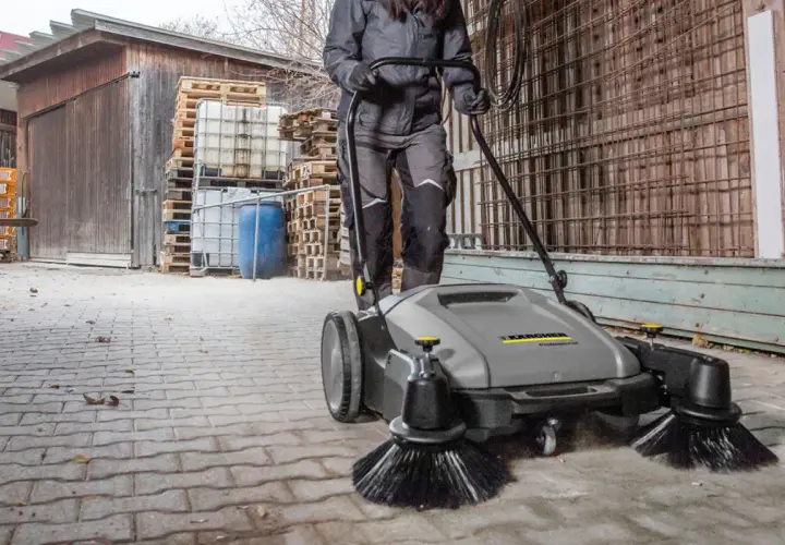 Osoba używa profesjonalnej zamiatarki do kostki brukowej Karcher, by szybko i skutecznie posprzątać teren.