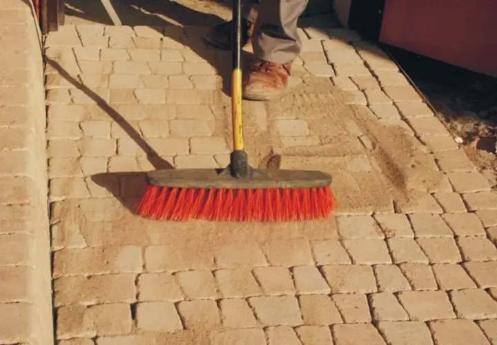 Szczotka z czerwonym włosiem usuwa piasek z kamiennej ścieżki, pokazując, jak usunąć igliwie z kamieni.