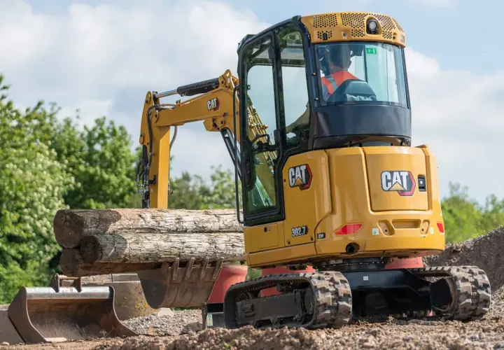 Minikoparka CAT 302.7 pracuje przy kopaniu fundamentów, podnosząc drewniane belki.
