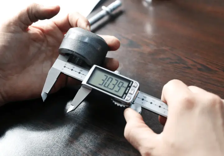 Precyzyjne pomiary: jak mierzyć mikrometrem. Dłoń trzymająca metalowy element i cyfrowy suwmiarkę, która pokazuje 30.39 mm.