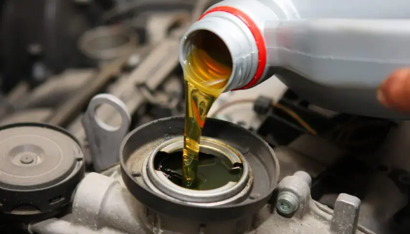 Wlewanie oleju do silnika Hatz Diesel. Płynny złoty olej spływa z szarej butelki do otworu silnika.