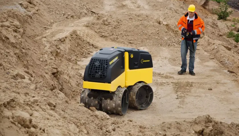 Na budowie pracuje operator z pilotem, sterując maszyną Bomag BMP 8500.