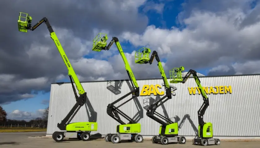 Cztery podnośniki koszowe Zoomlion w jaskrawej zieleni stoją przed budynkiem z napisem "BAC WYNAJEM".