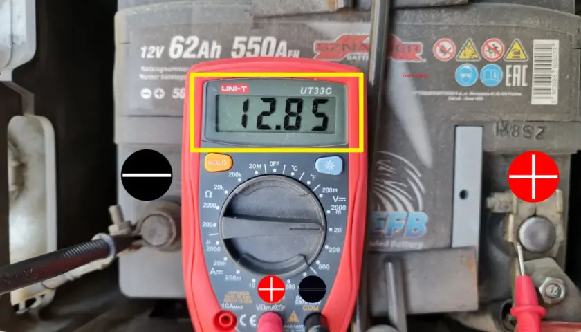 Multimetr pokazuje 12.85V, co jest wynikiem pomiaru napięcia elektrycznego akumulatora samochodowego.