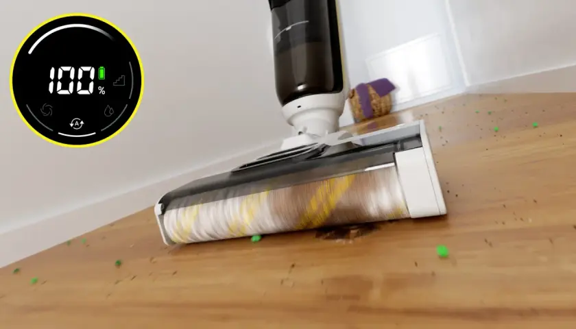 Odkurzacz Karcher z obrotową szczotką zbiera zielone kuleczki i brud z drewnianej podłogi. Wyświetlacz pokazuje 100% baterii.