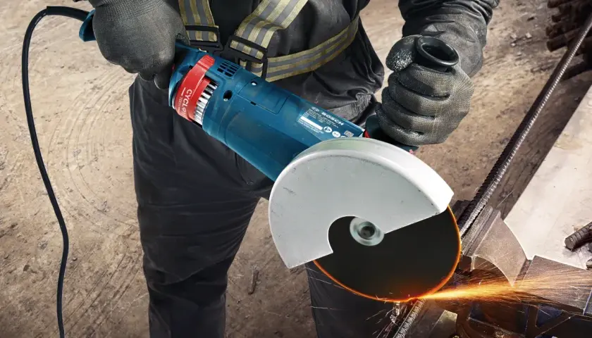 Pracownik w rękawicach zakłada tarczę na szlifierkę kątową Bosch, przygotowując się do cięcia metalu. Iskry sypią się podczas pracy.