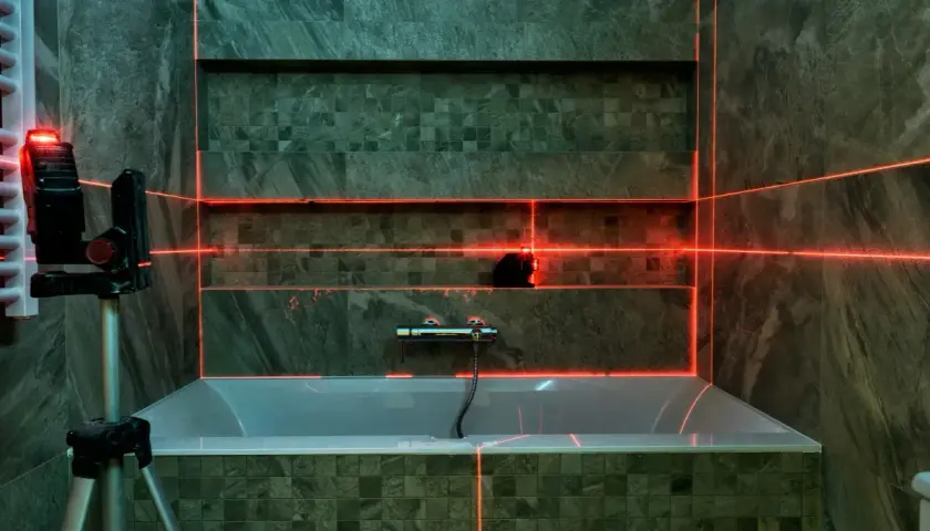 Laser krzyżowy wyznacza linie, pomagając jak wyznaczyć kąt prosty na podłodze. W łazience z wanną i nowoczesnymi płytkami.