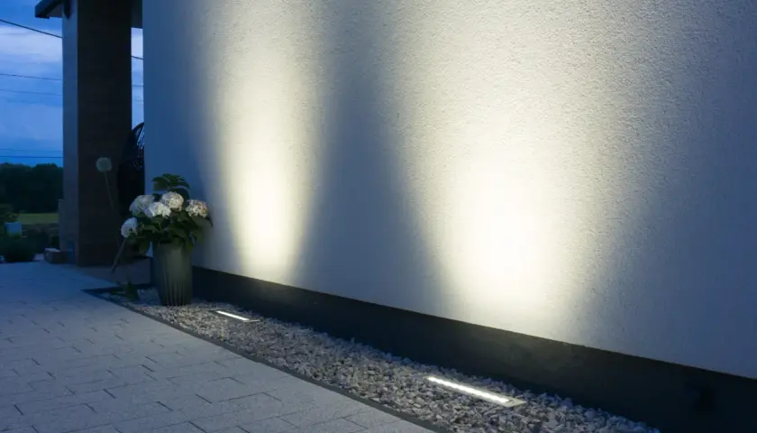 Nowoczesne oświetlenie placu budowy podkreśla architekturę domu. Dyskretne lampy wbudowane w żwir i podjazd tworzą nastrojową atmosferę.
