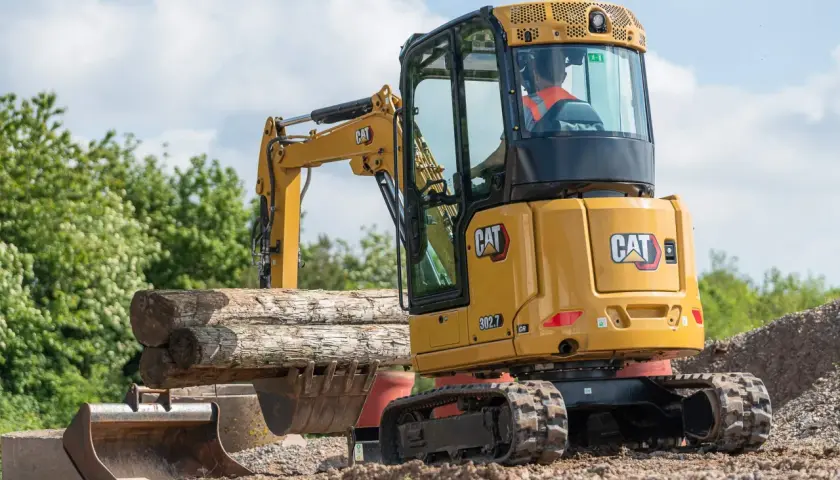 Minikoparka CAT 302.7 pracuje przy kopaniu fundamentów, podnosząc drewniane belki.