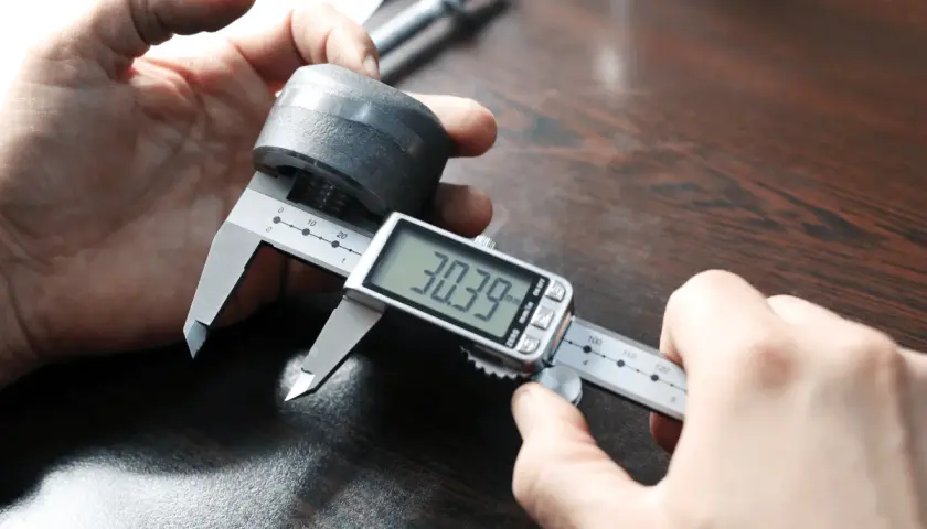 Precyzyjne pomiary: jak mierzyć mikrometrem. Dłoń trzymająca metalowy element i cyfrowy suwmiarkę, która pokazuje 30.39 mm.
