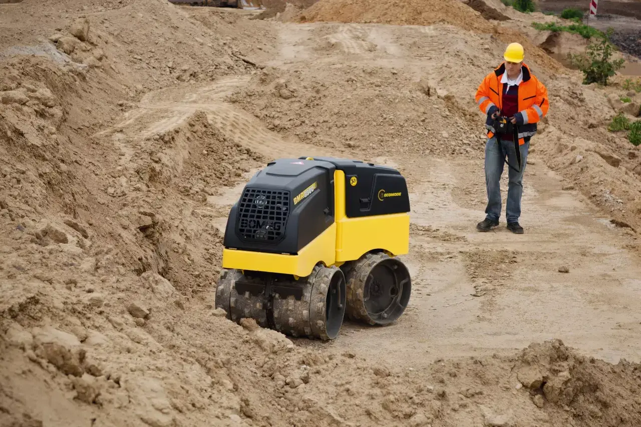 Na budowie pracuje operator z pilotem, sterując maszyną Bomag BMP 8500.