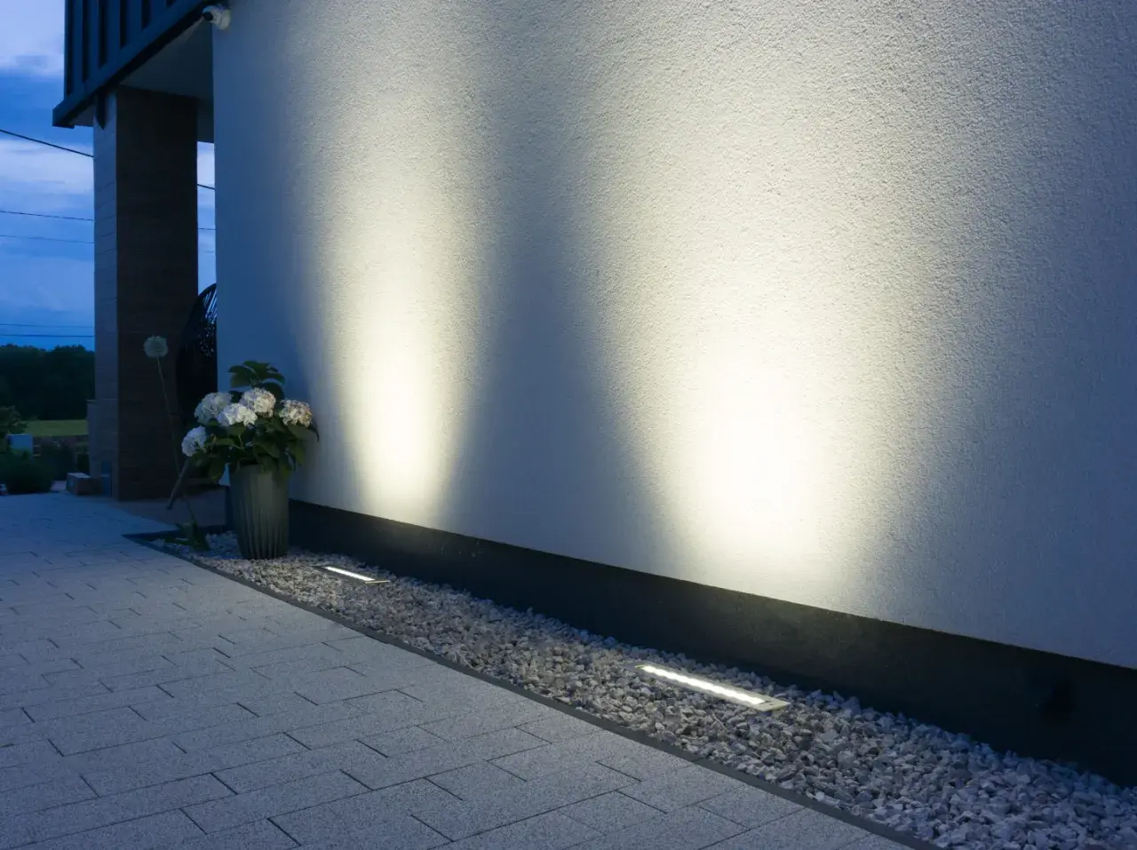 Nowoczesne oświetlenie placu budowy podkreśla architekturę domu. Dyskretne lampy wbudowane w żwir i podjazd tworzą nastrojową atmosferę.