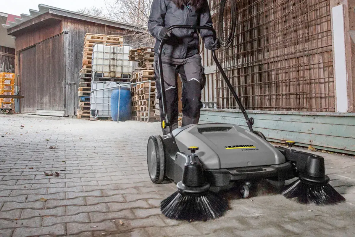 Osoba używa profesjonalnej zamiatarki do kostki brukowej Karcher, by szybko i skutecznie posprzątać teren.