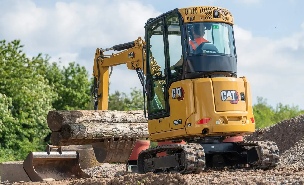 Minikoparka CAT 302.7 pracuje przy kopaniu fundamentów, podnosząc drewniane belki.